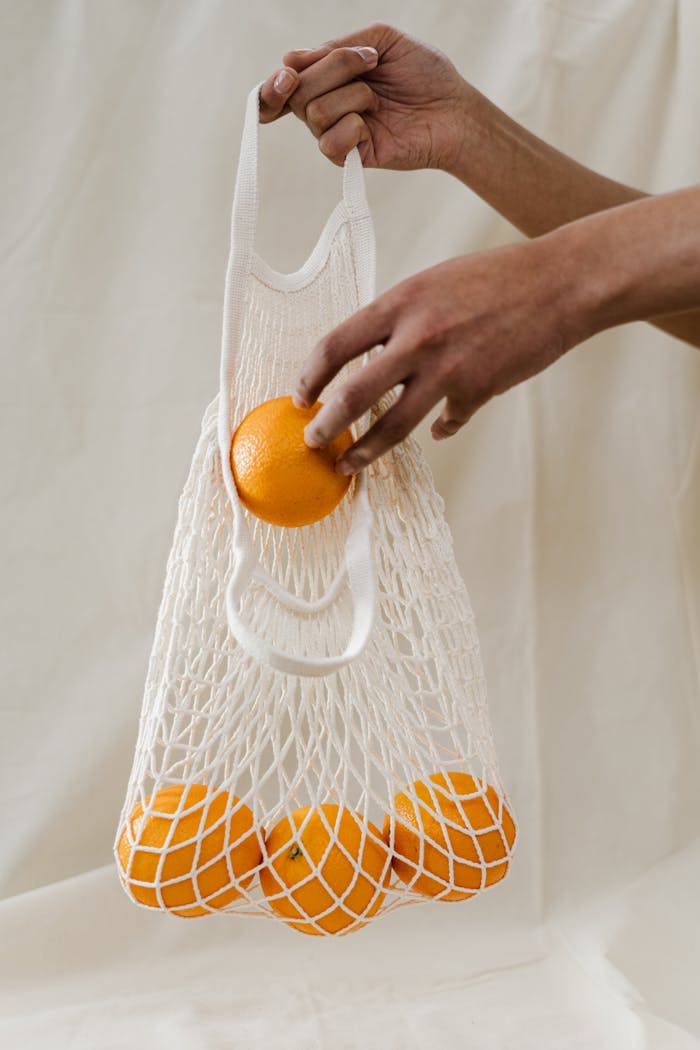 Hand holding a reusable mesh bag filled with fresh oranges, promoting sustainability and zero waste shopping.